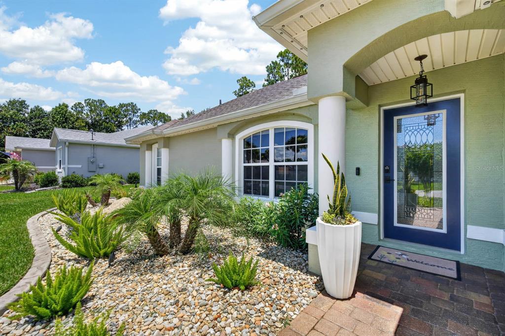 The exterior of a light green house features a blue front door and rock landscaping — 98 WESTGRILL DRIVE, PALM COAST, FL