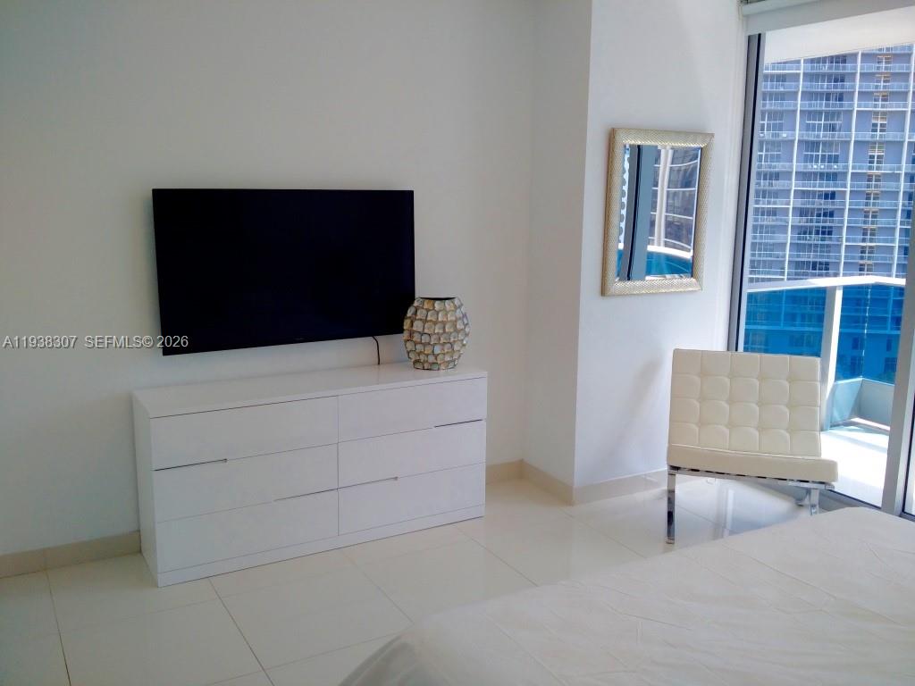A bedroom features a white dresser, a wall-mounted television, a white chair, and a balcony — 200 Biscayne Boulevard Way # 906, Miami FL 33131, MIAMI, FL