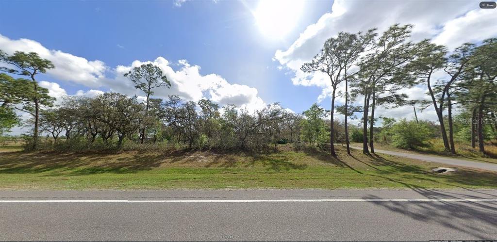 A paved road runs in front of a grassy, wooded vacant lot under a sunny sky — COMMONWEALTH AVENUE N, POLK CITY, FL