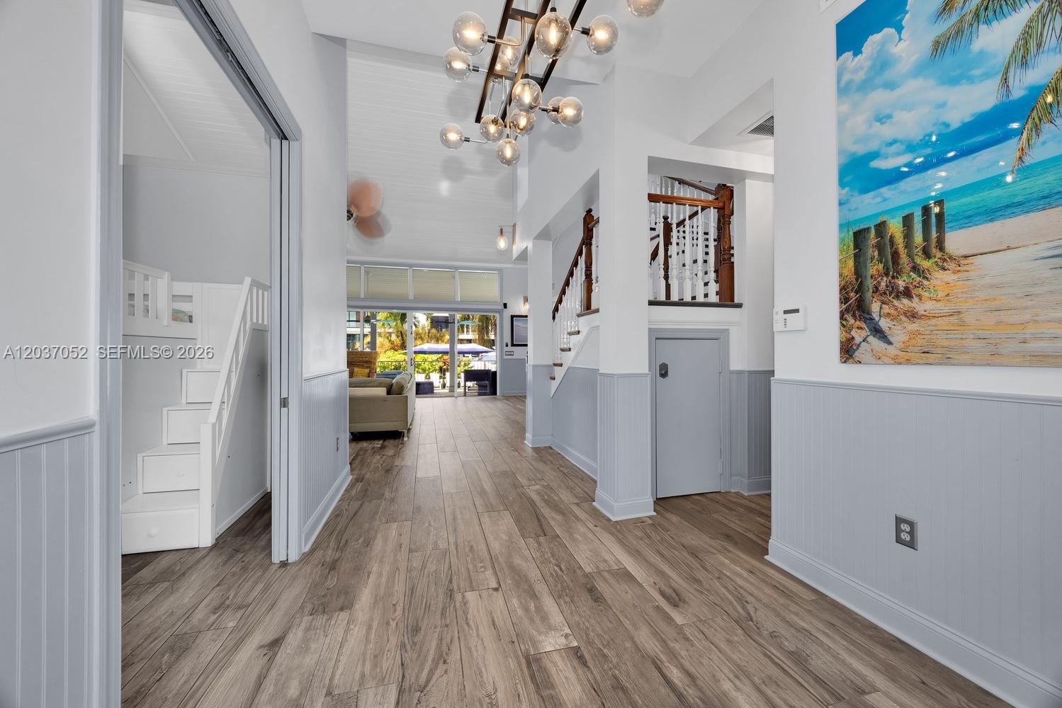 A bright hallway features wood-look flooring, wainscoting, a modern chandelier, and a staircase — 1074 NE Little River Dr, Miami FL 33138, MIAMI, FL