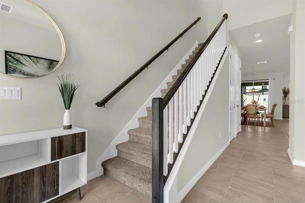 A carpeted staircase with a wooden handrail sits beside a white console table and mirror — 1676 TROPICAL PALMS CIRCLE, KISSIMMEE, FL