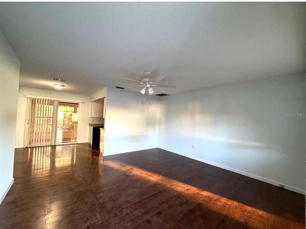 A living room with dark wood-look flooring, a ceiling fan, and sliding glass doors — 11248 SW 76TH TERRACE, OCALA, FL