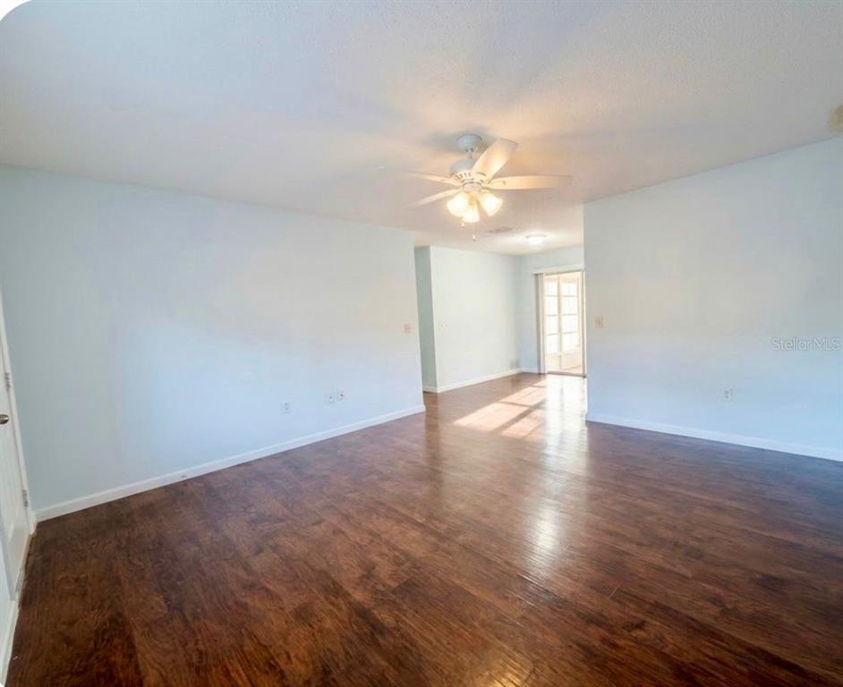 An empty room with light blue walls, dark wood-look flooring, and a ceiling fan — 11248 SW 76TH TERRACE, OCALA, FL