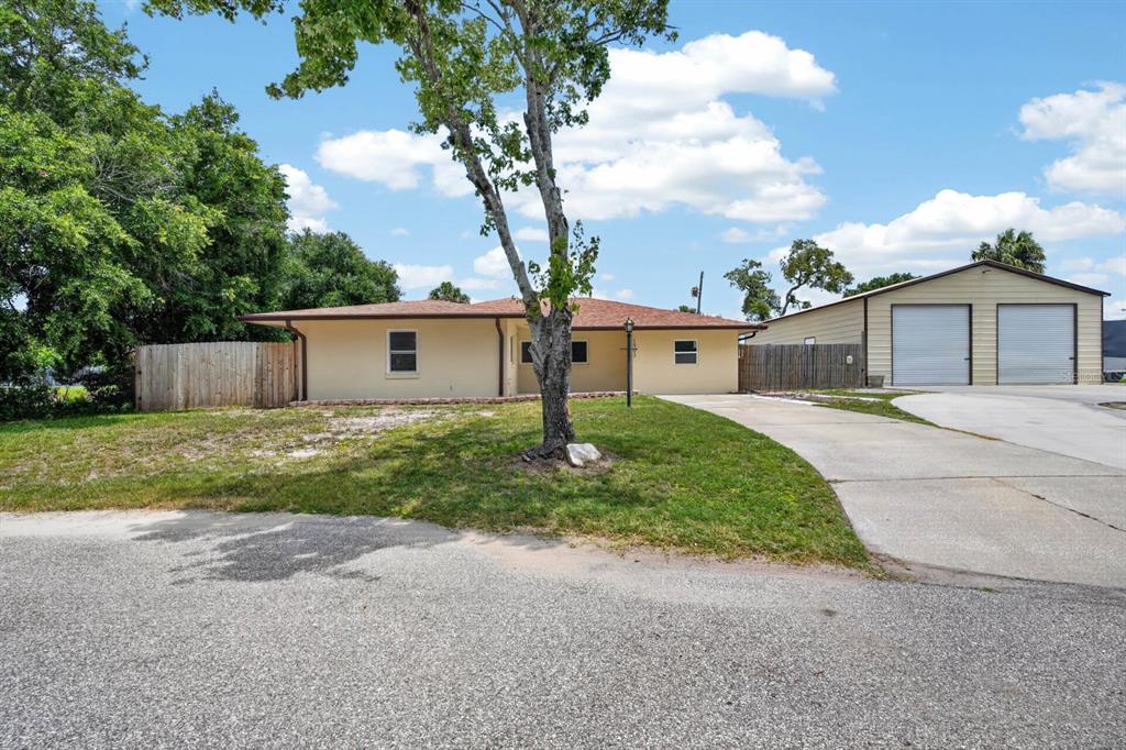 A single-story house with a tan exterior, a brown roof, and a detached metal garage — 1803 EVERGREEN DRIVE, EDGEWATER, FL