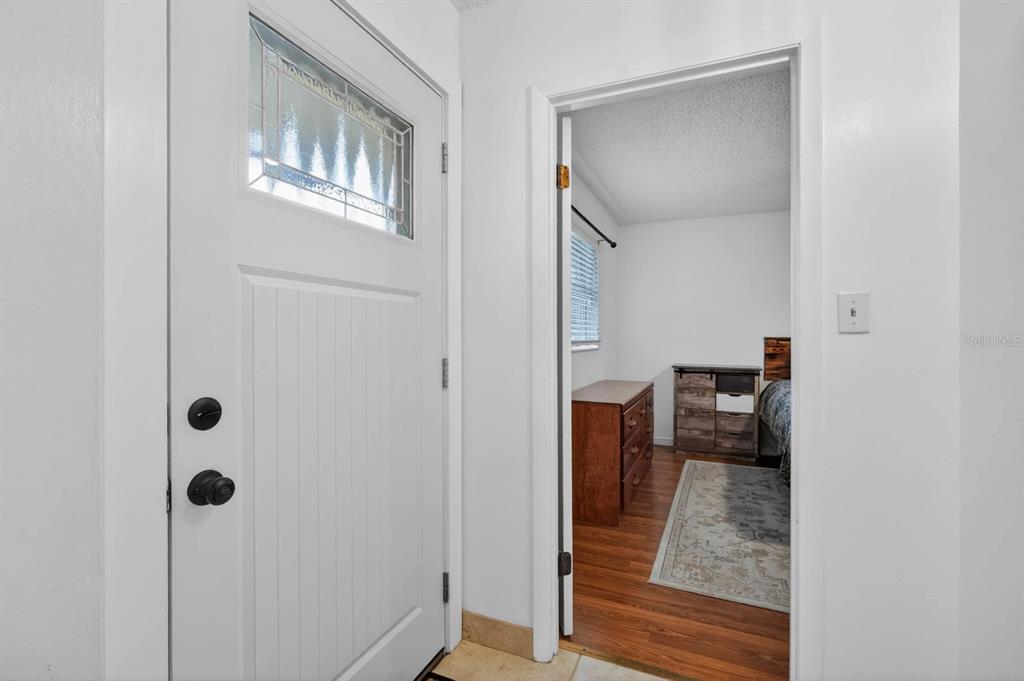 A white front door with a glass insert opens into a hallway leading to a bedroom — 1803 EVERGREEN DRIVE, EDGEWATER, FL