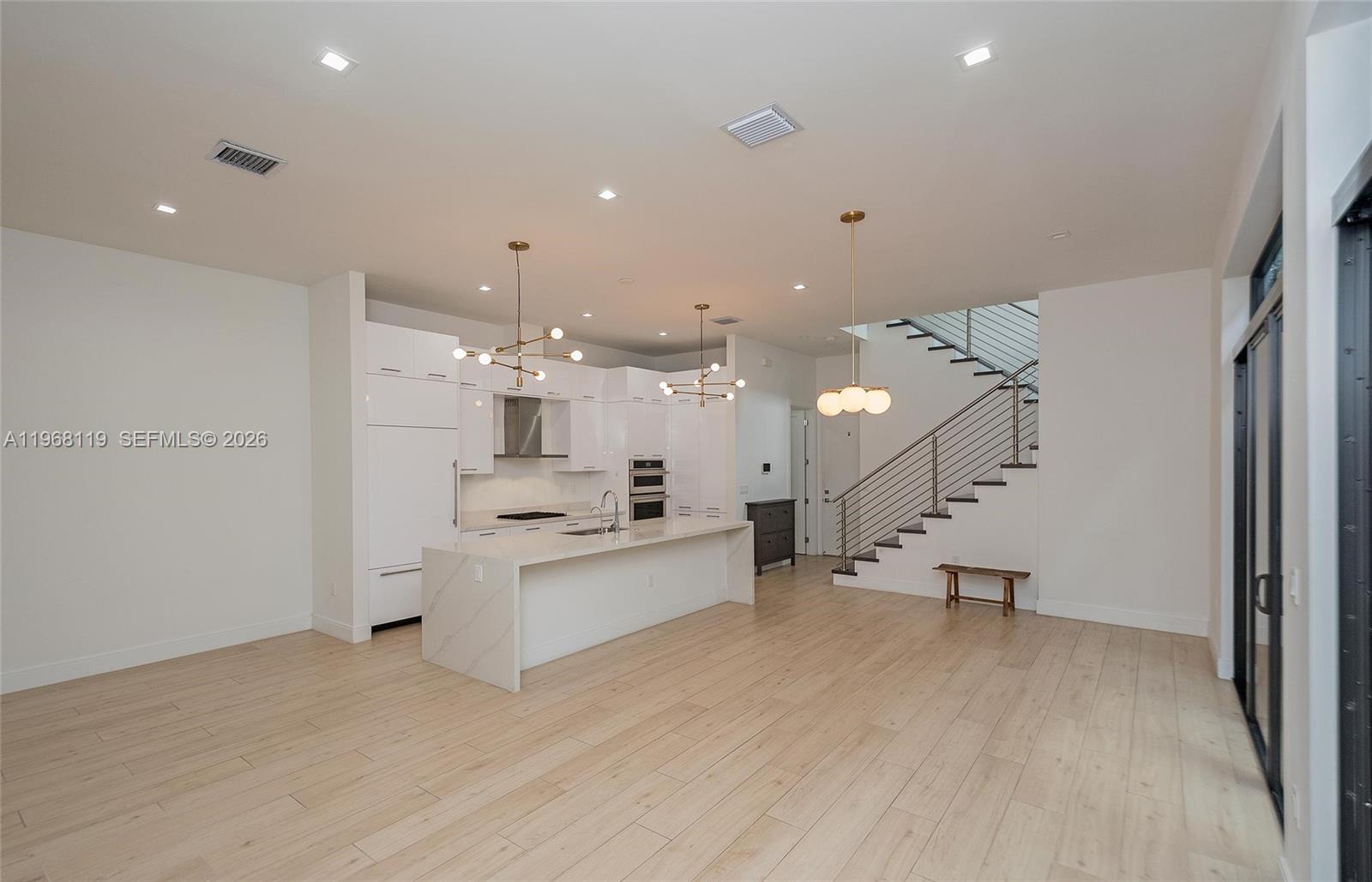 A modern kitchen with white cabinetry and a marble island sits beside a staircase — 4454 NW 80th Ave, Doral FL 33166, DORAL, FL