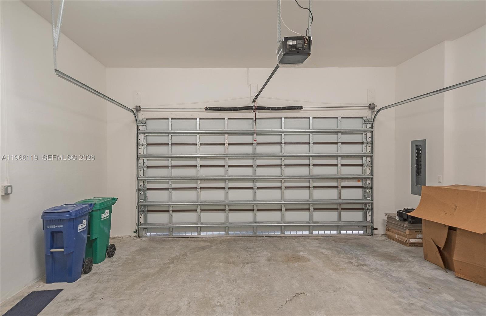 An empty garage features a sectional door, concrete flooring, and two plastic waste bins — 4454 NW 80th Ave, Doral FL 33166, DORAL, FL