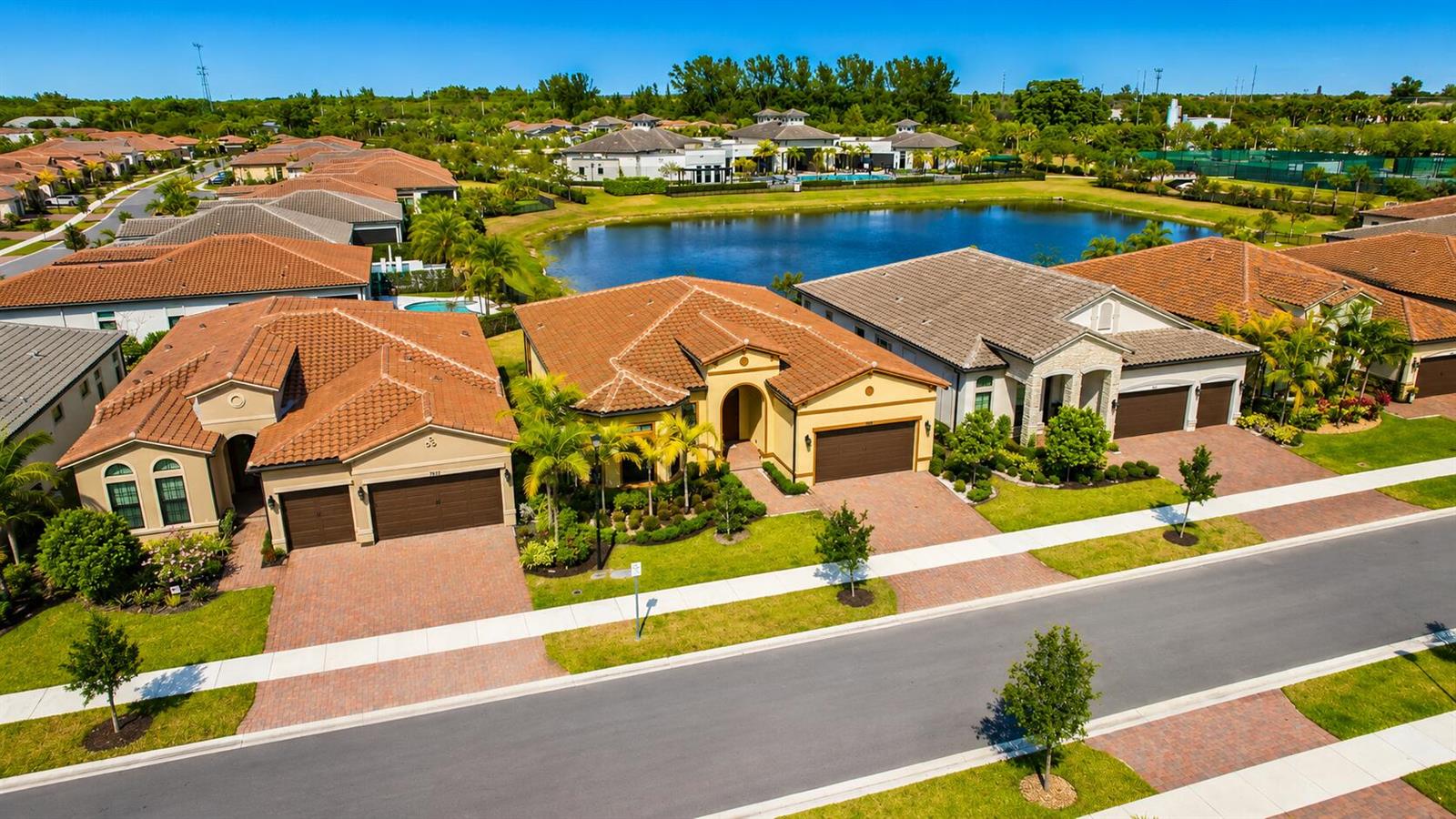 An aerial view shows several suburban houses with tiled roofs situated near a central lake — 7818 Rowan Terrace, Parkland FL 33067, PARKLAND, FL