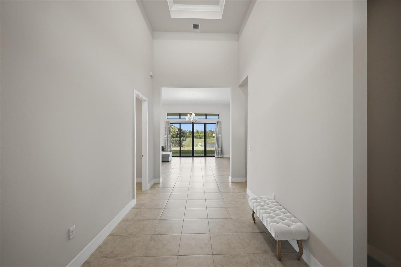 A long, tiled entryway leads to a living area with large glass doors overlooking a lake — 7818 Rowan Terrace, Parkland FL 33067, PARKLAND, FL