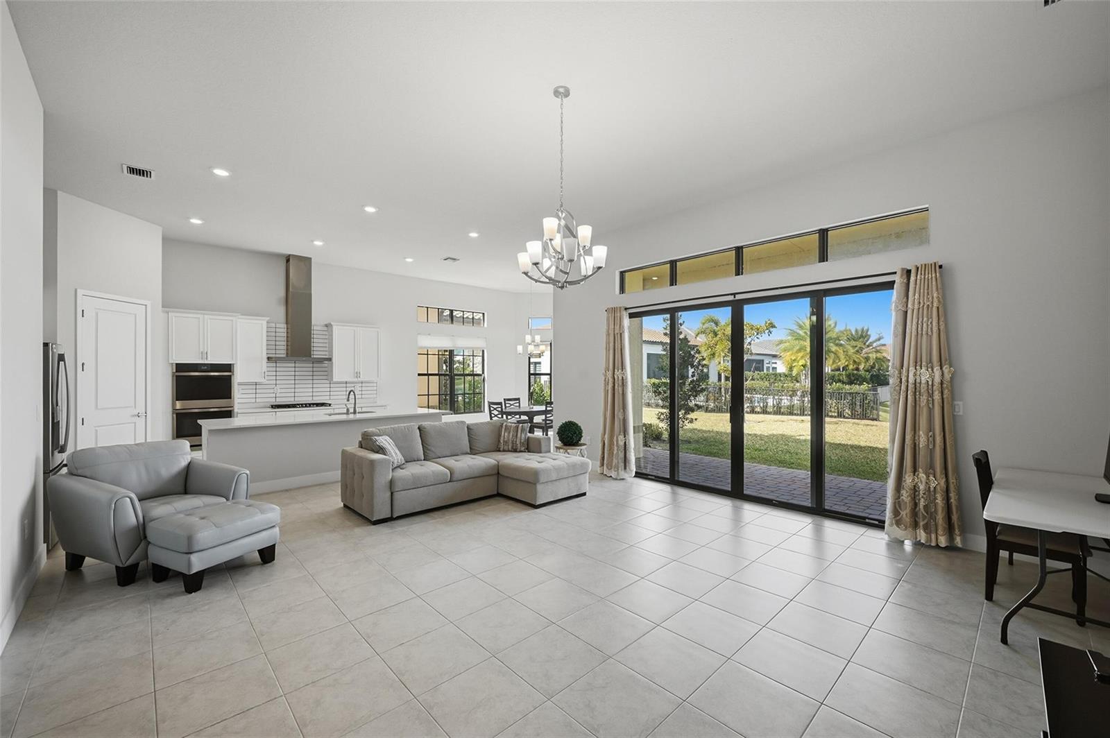A bright open-concept living room features tile flooring, a gray sectional, and large sliding doors — 7818 Rowan Terrace, Parkland FL 33067, PARKLAND, FL