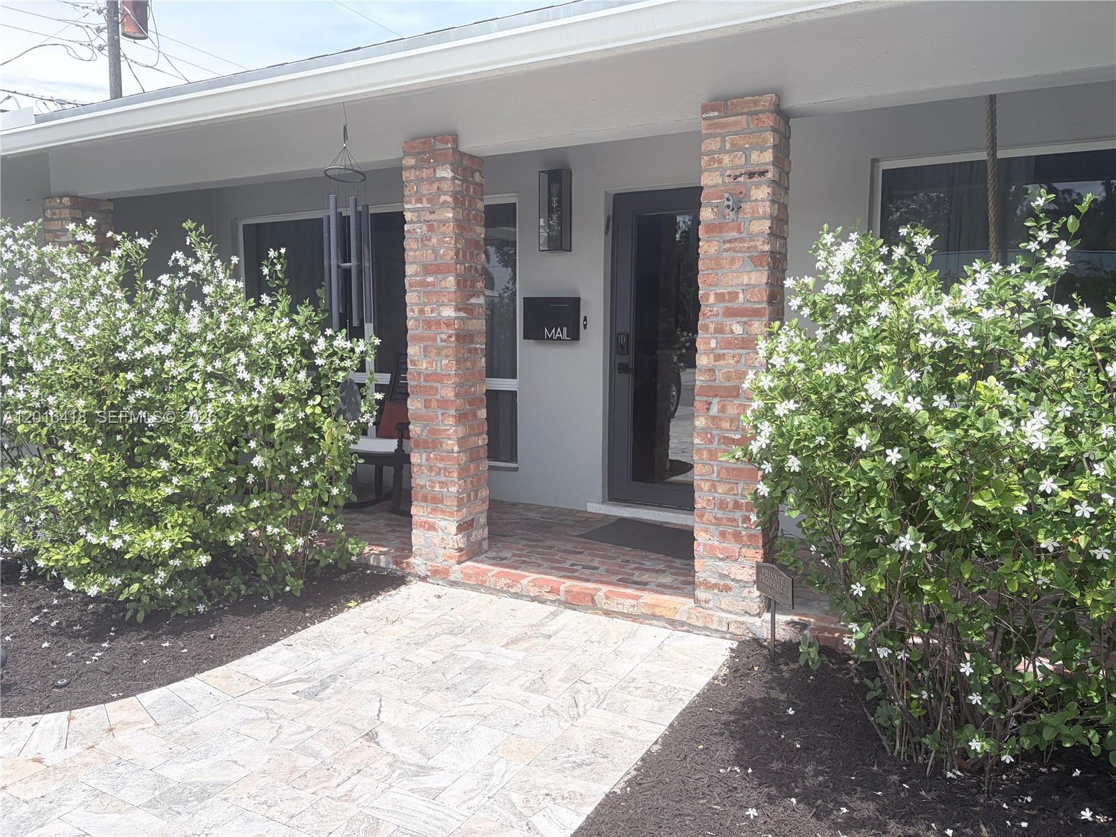 A brick-columned front porch features a stone walkway and two large flowering bushes — 1705 NE 24th St, Wilton Manors FL 33305, WILTON MANORS, FL