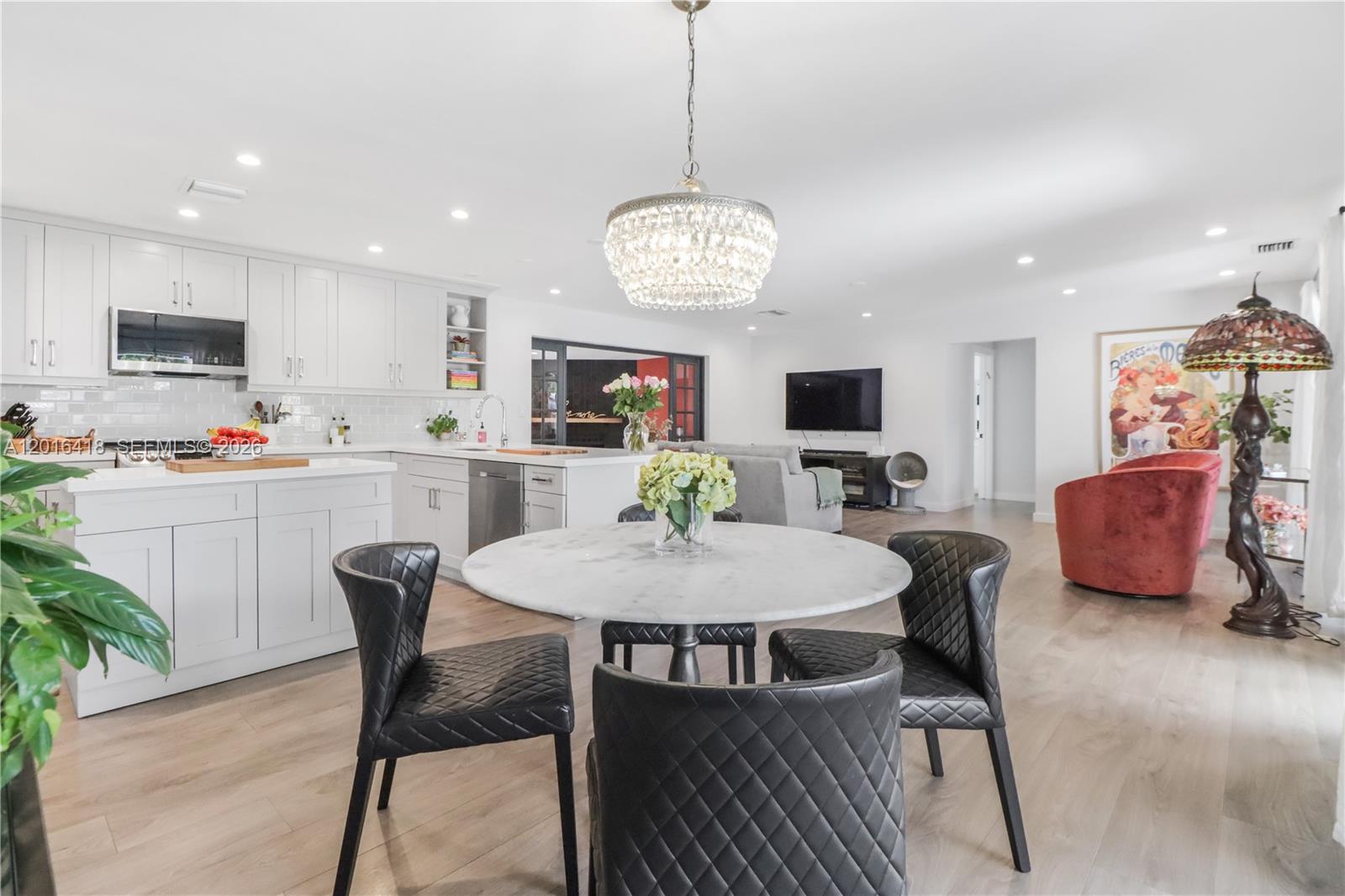 A bright open-concept kitchen and dining area features white cabinetry, a marble table, and chandelier — 1705 NE 24th St, Wilton Manors FL 33305, WILTON MANORS, FL