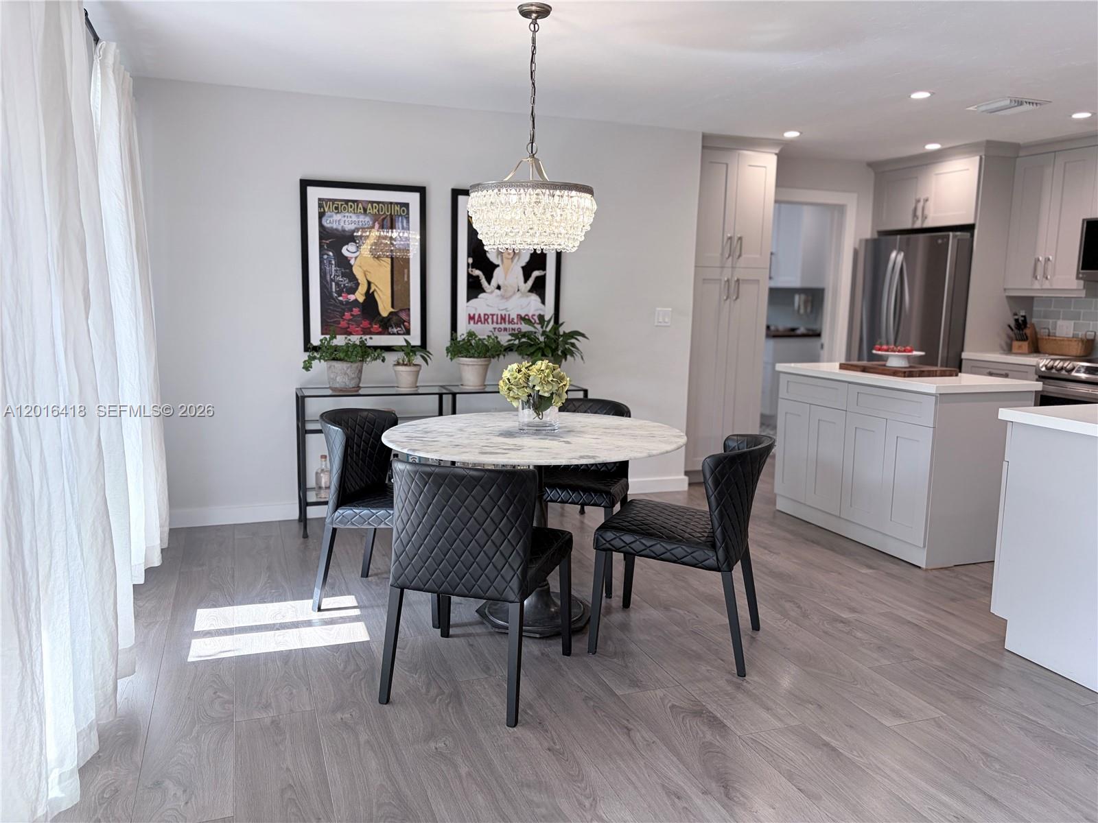 A dining area features a round marble table, black quilted chairs, and a crystal chandelier — 1705 NE 24th St, Wilton Manors FL 33305, WILTON MANORS, FL
