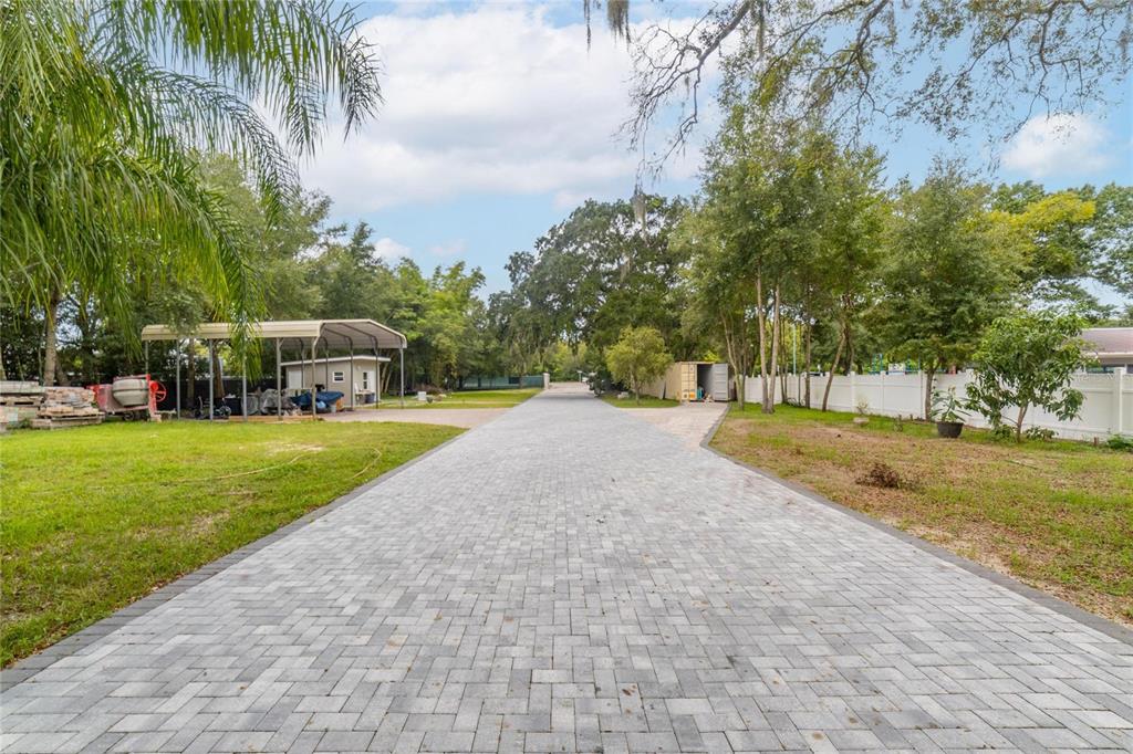 A long paved driveway leads through a grassy yard toward a metal carport and trees — 201 S LAKEWOOD DRIVE, BRANDON, FL