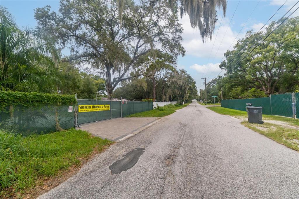 A paved road leads past a fenced property with a gated entrance and large trees — 201 S LAKEWOOD DRIVE, BRANDON, FL