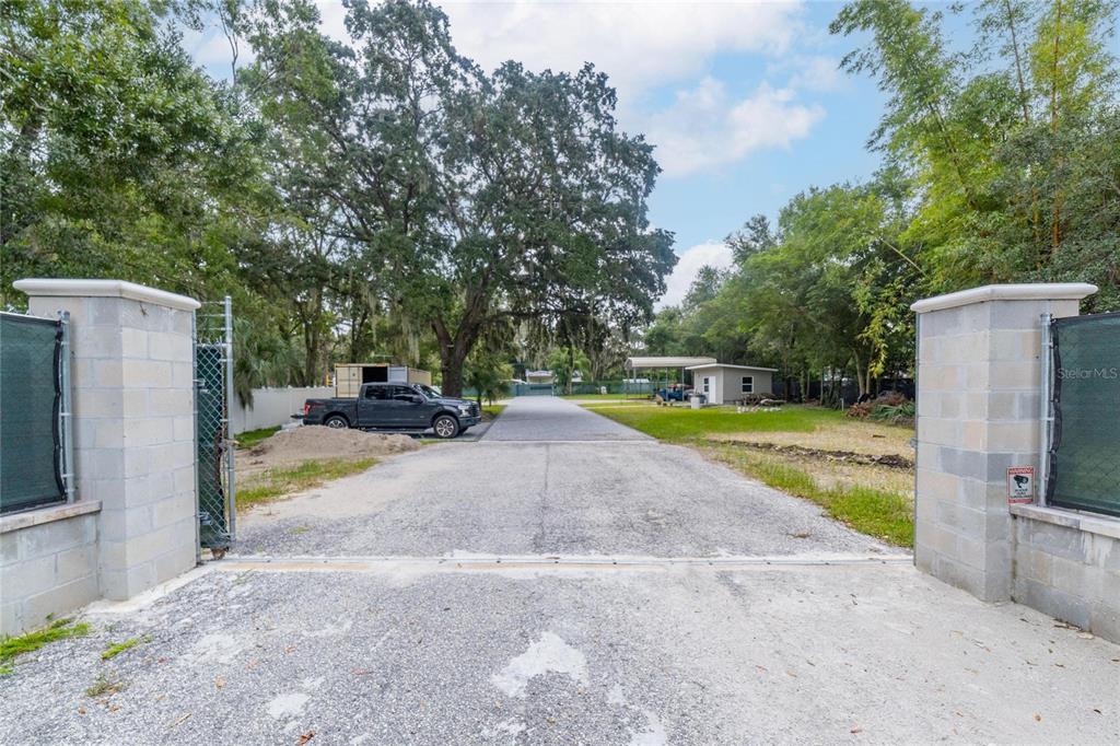 A gravel driveway leads through a gated entrance toward a small building and trees — 201 S LAKEWOOD DRIVE, BRANDON, FL
