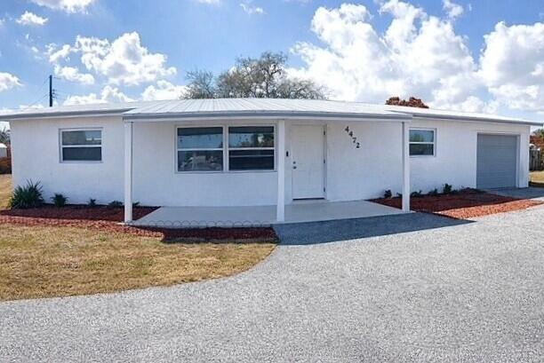 A white single-story house with a metal roof, front porch, and gravel driveway — 4472 SE Alden Avenue, Stuart FL 34997, STUART, FL