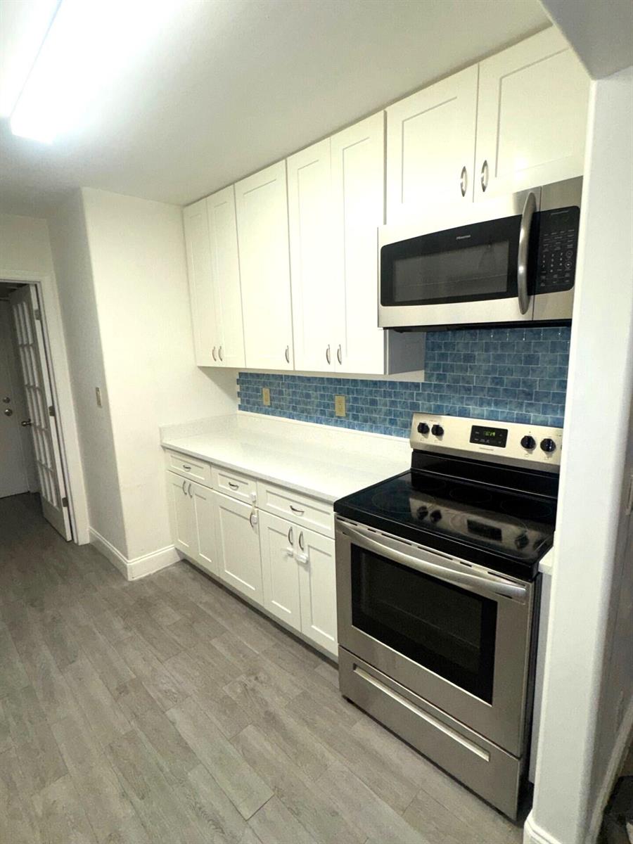 A kitchen features white cabinets, a blue tile backsplash, stainless steel appliances, and gray flooring — 4472 SE Alden Avenue, Stuart FL 34997, STUART, FL