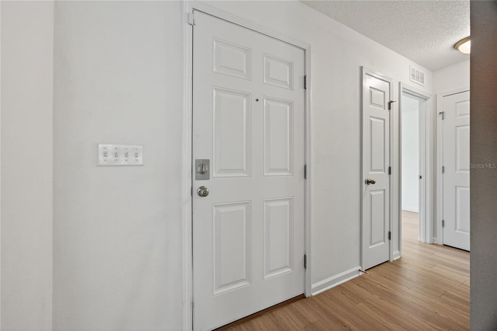 A white entry door with a deadbolt is positioned next to a hallway with wood-look flooring — 5315 COLONIAL AVENUE, JACKSONVILLE, FL