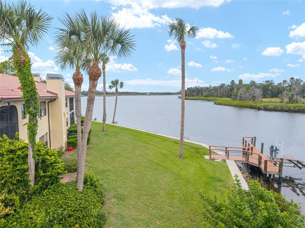 An exterior view of a waterfront building with a lawn, palm trees, and a wooden dock — 362 NW 14TH PLACE UNIT 21, CRYSTAL RIVER, FL
