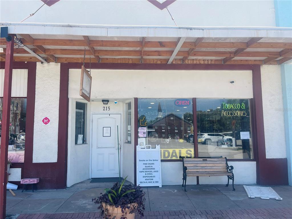 The exterior of a commercial storefront features a white door, large windows, and a wooden bench — 215 W OAK STREET, ARCADIA, FL