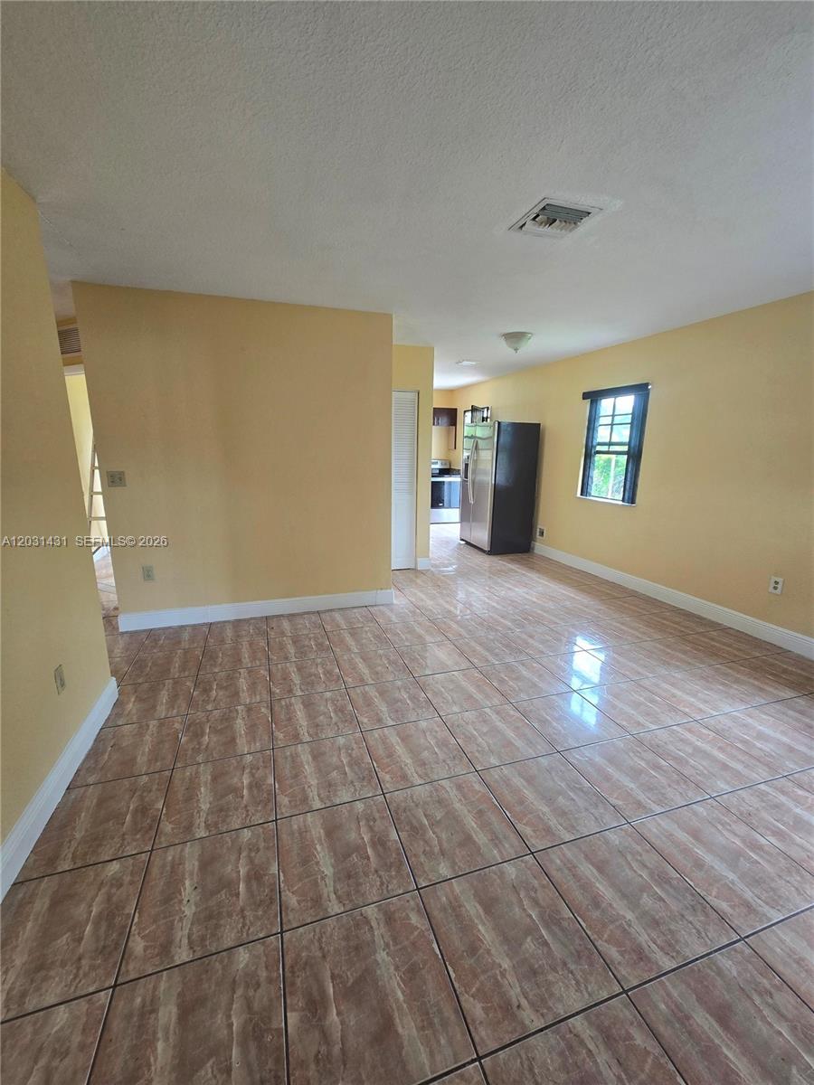 A room with light yellow walls and brown tile flooring leads to a kitchen area — 313 NW 97th St # 313, Miami FL 33150, MIAMI, FL