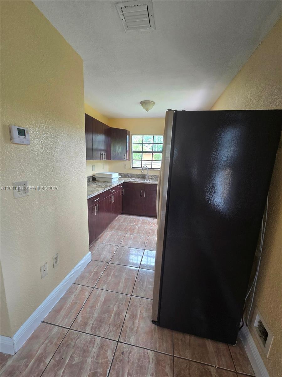 A kitchen features dark wood cabinets, granite countertops, tile flooring, and a black refrigerator — 313 NW 97th St # 313, Miami FL 33150, MIAMI, FL