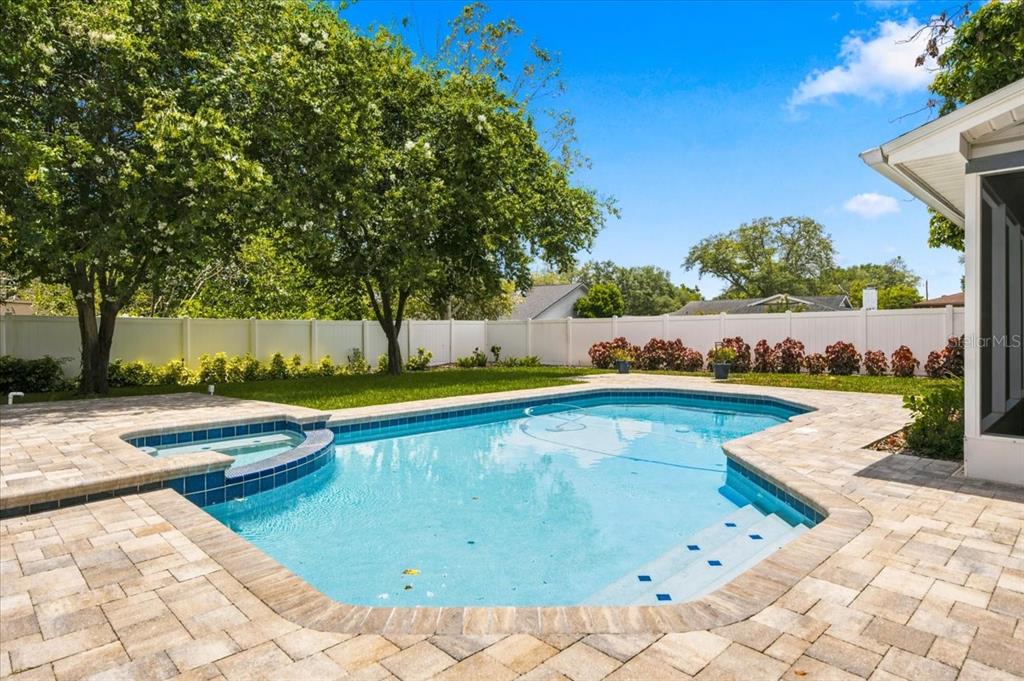 A backyard features a swimming pool with a spa, stone pavers, and a white fence — 13101 BURNES LAKE DRIVE, TAMPA, FL