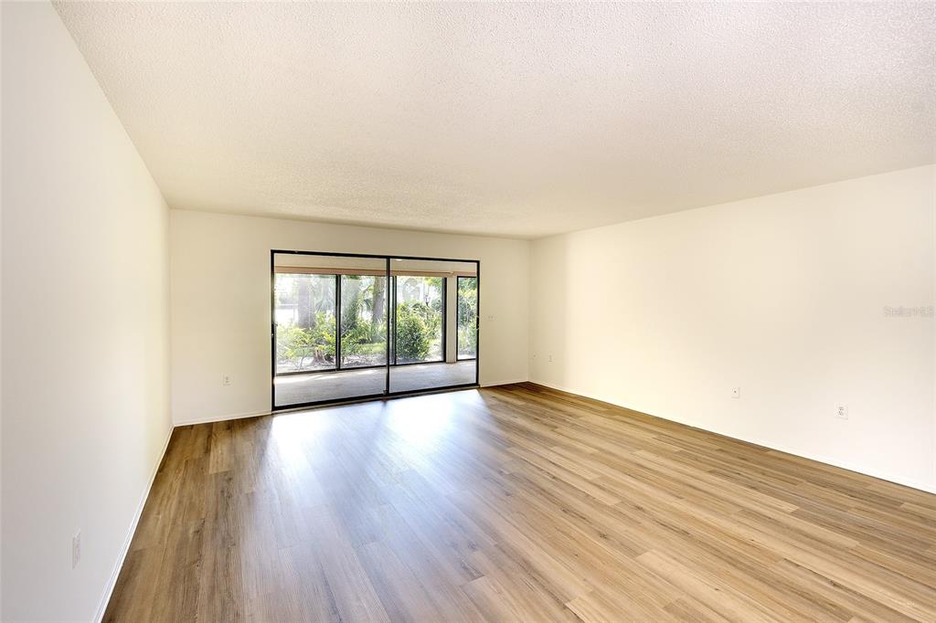 An empty living room features light wood-look flooring, white walls, and sliding glass patio doors — 123 WILD PALM DRIVE UNIT 123, BRADENTON, FL