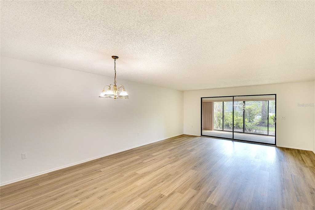 An empty room with light wood-look flooring, a hanging light fixture, and sliding glass doors — 123 WILD PALM DRIVE UNIT 123, BRADENTON, FL
