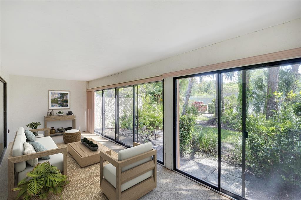 A sunroom features light-colored furniture, a textured rug, and large sliding glass doors overlooking greenery — 123 WILD PALM DRIVE UNIT 123, BRADENTON, FL