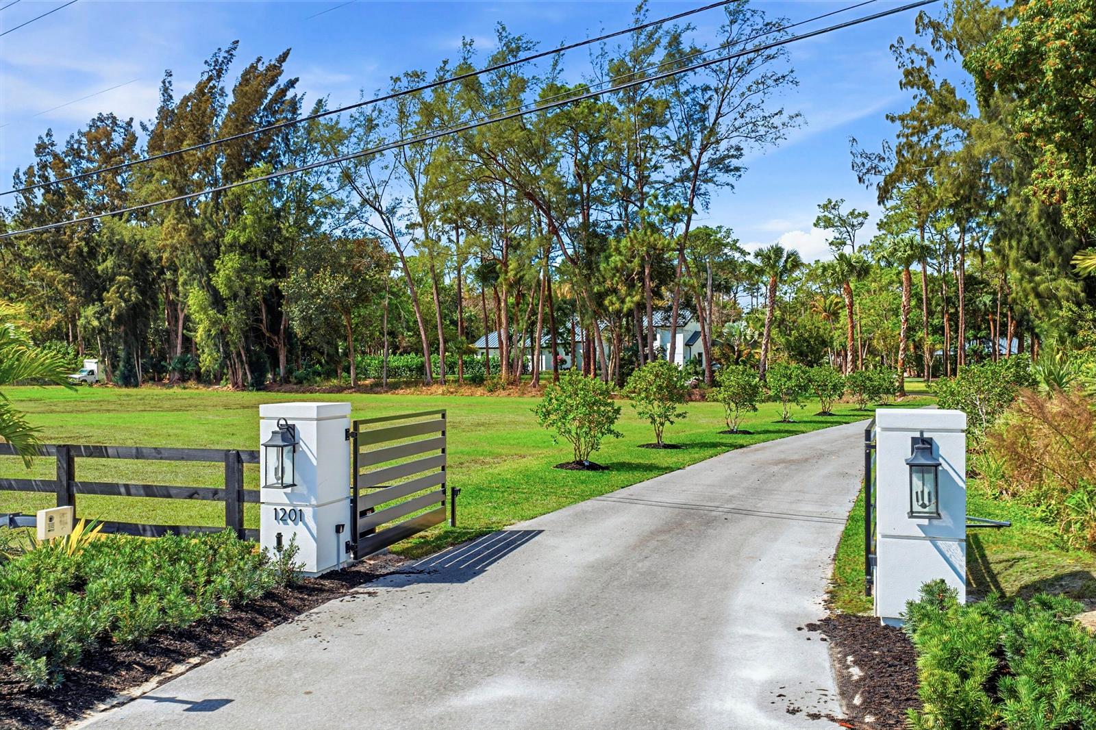 A paved driveway leads through a gated entrance with white pillars toward a distant house — 1201 F Road, FL 33470, FL