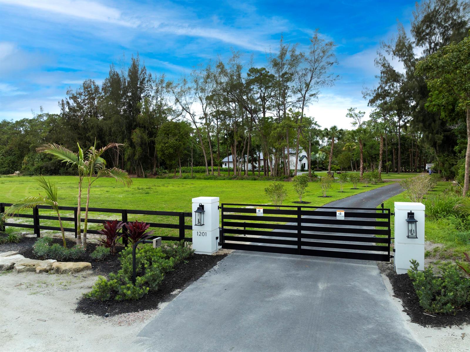 A black metal gate and fence enclose a driveway leading to a house and trees — 1201 F Road, FL 33470, FL