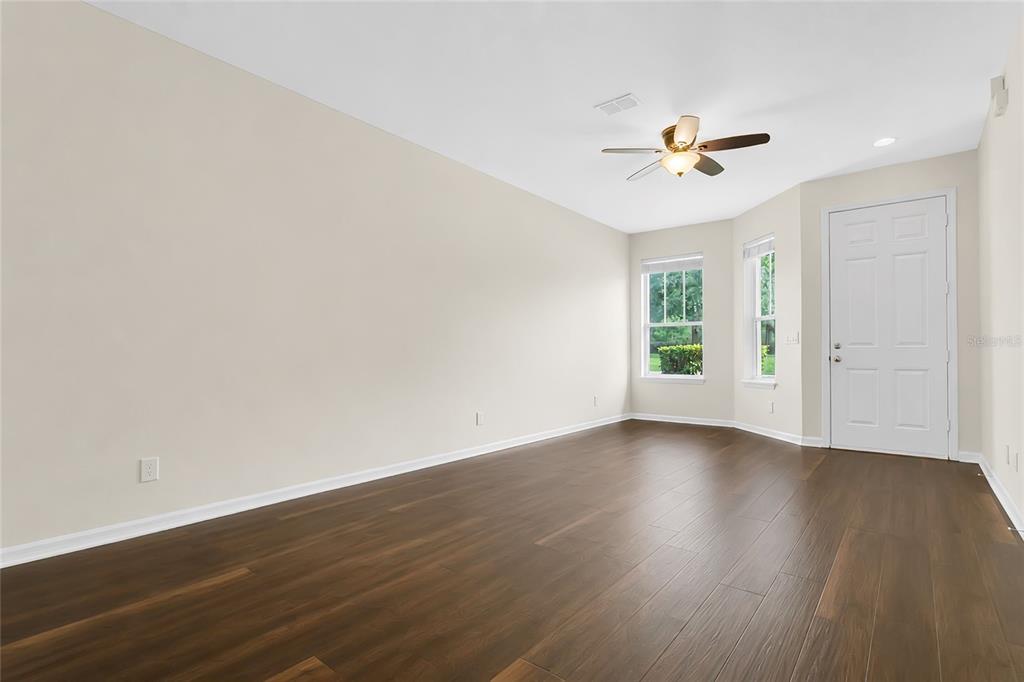An empty room features dark wood-look flooring, beige walls, a ceiling fan, and a white door — 34346 TUSCANY AVENUE, SORRENTO, FL
