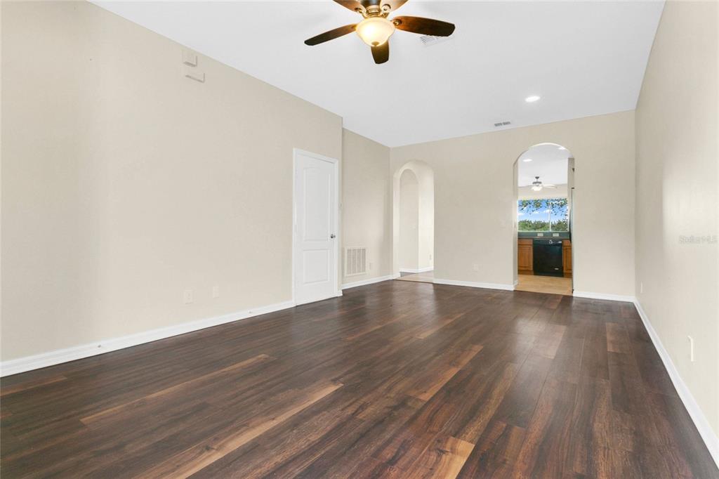 An empty room with dark wood-look flooring, beige walls, a ceiling fan, and arched doorways — 34346 TUSCANY AVENUE, SORRENTO, FL