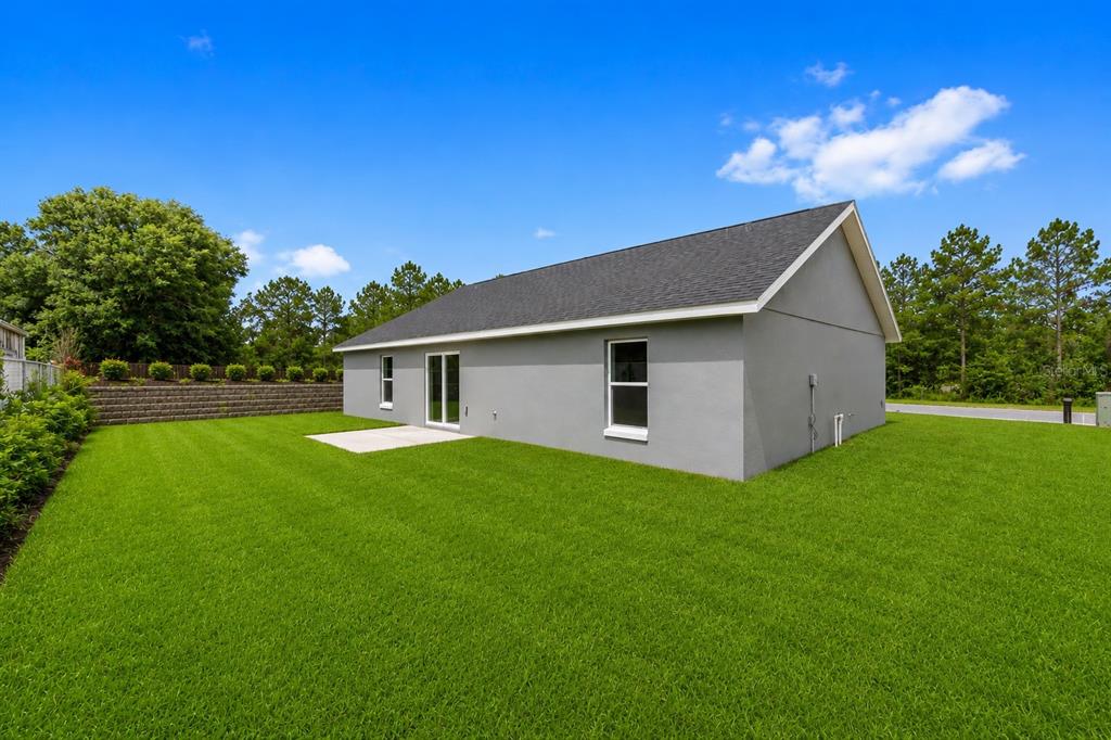 The exterior of a gray single-story house features a small concrete patio and green lawn — 19788 SW FLAMINGO DRIVE, DUNNELLON, FL