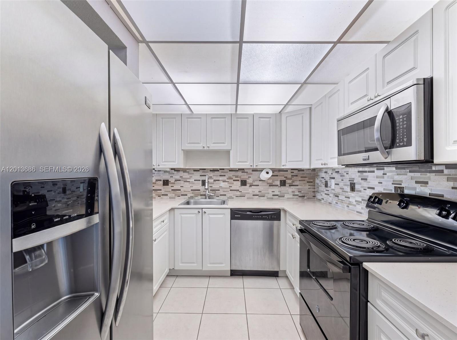 A kitchen features white cabinets, stainless steel appliances, a tiled backsplash, and a drop ceiling — 6950 Miami Gardens Dr # 506, Hialeah FL 33015, HIALEAH, FL