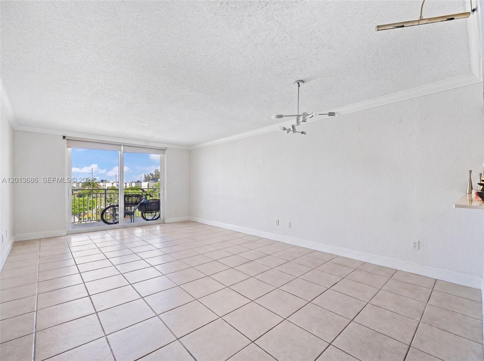 An empty living room features white walls, tile flooring, a modern chandelier, and a balcony — 6950 Miami Gardens Dr # 506, Hialeah FL 33015, HIALEAH, FL