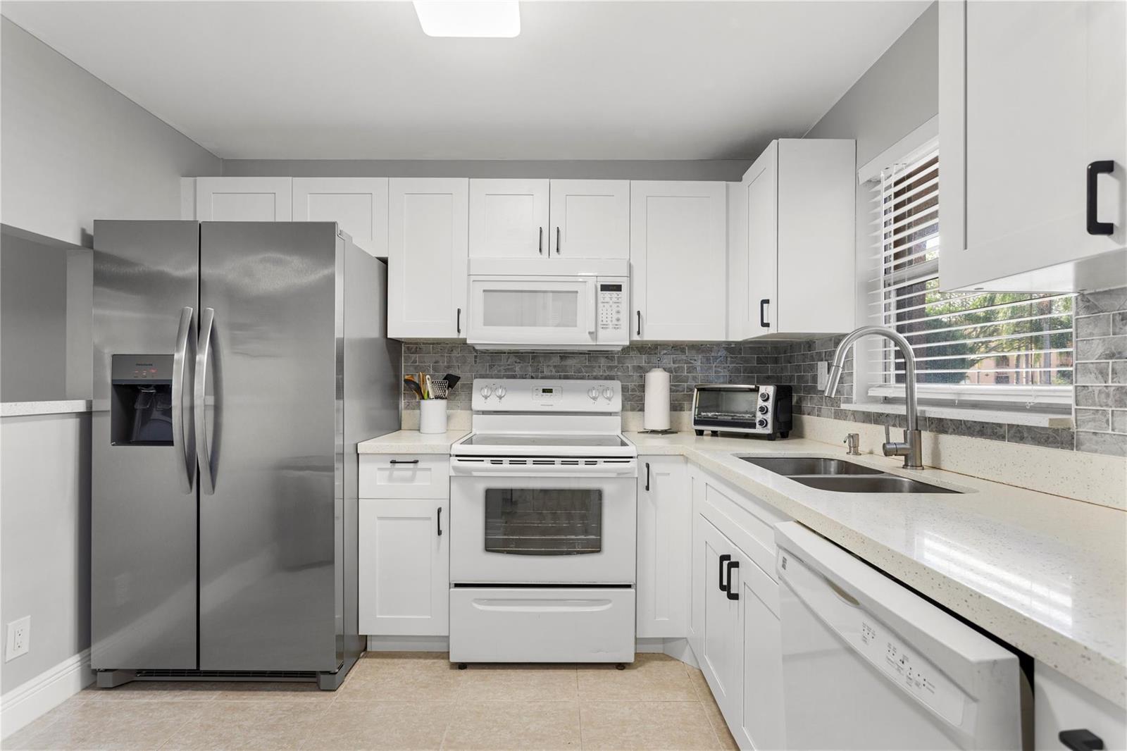 A kitchen with white cabinets, stainless steel refrigerator, white stove, and light-colored countertops — 9700 Sunrise Lakes Boulevard # 101, Sunrise FL 33322, SUNRISE, FL