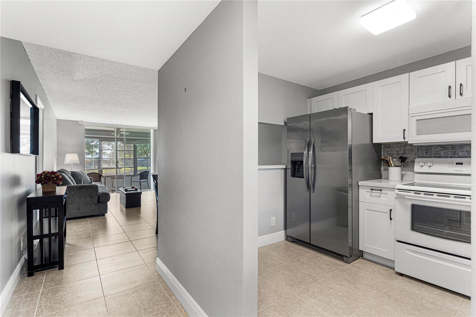 A kitchen with white cabinets and stainless steel appliances opens into a living room area — 9700 Sunrise Lakes Boulevard # 101, Sunrise FL 33322, SUNRISE, FL