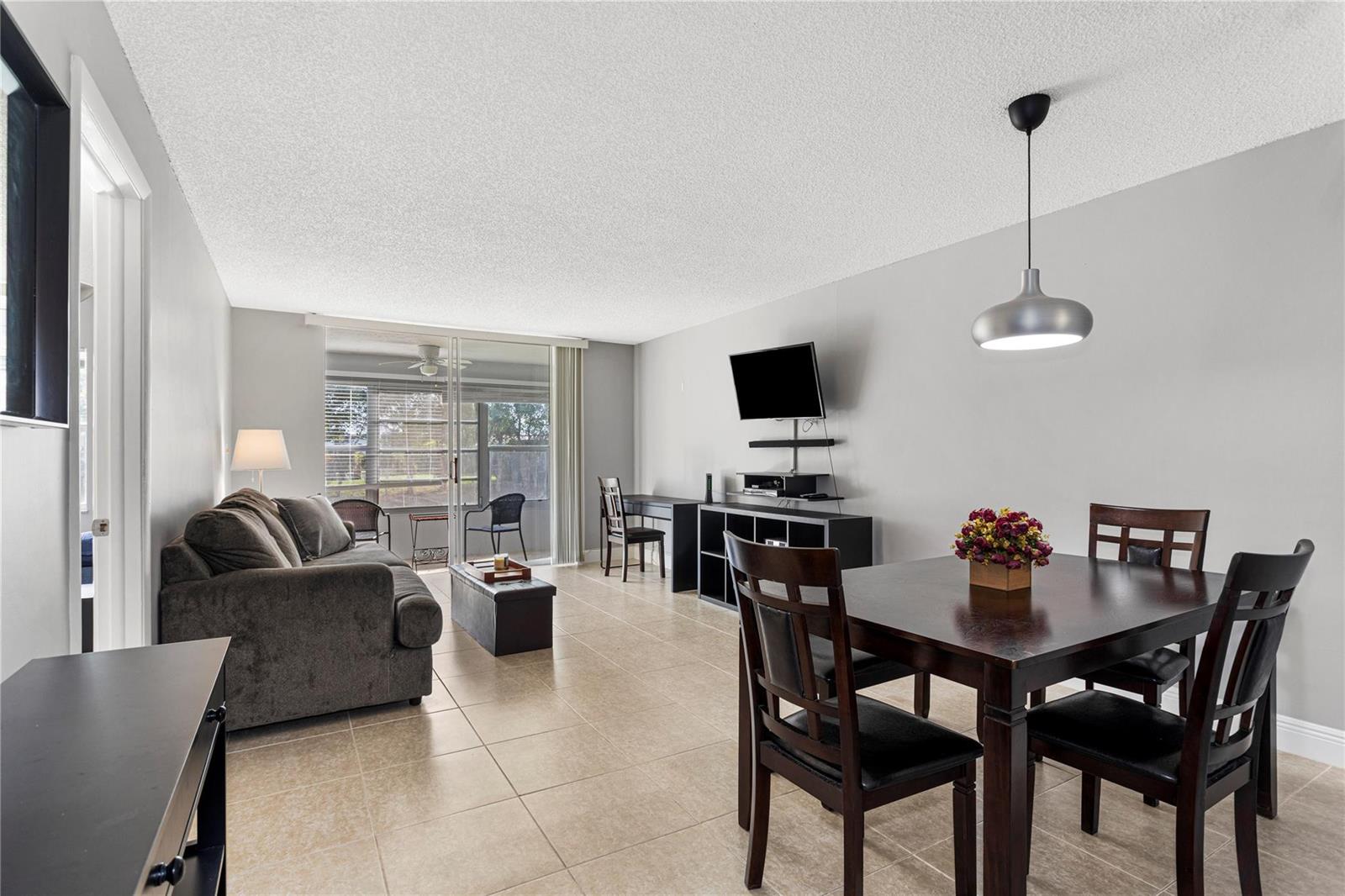 This open-concept living and dining area features tile flooring, a ceiling pendant light, and balcony access — 9700 Sunrise Lakes Boulevard # 101, Sunrise FL 33322, SUNRISE, FL