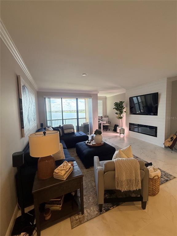 A living room features a dark sectional, fireplace, wall-mounted television, and a balcony overlooking water — 16300 COUNTY ROAD 455 UNIT 604, MONTVERDE, FL