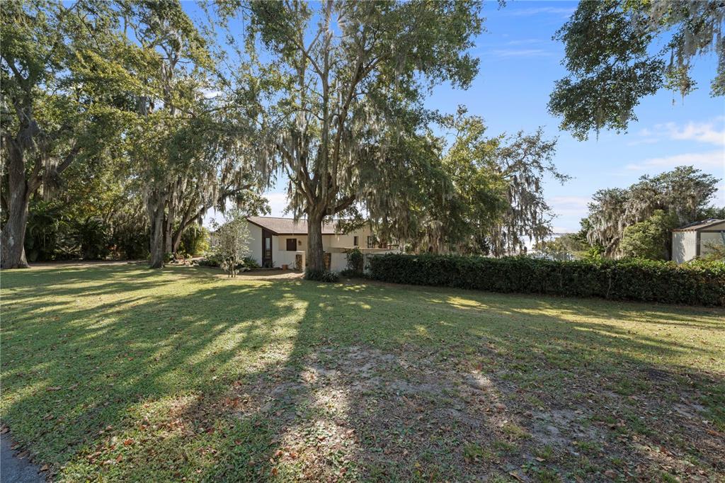 A house with a brown roof sits behind a large lawn and mature oak trees — 11210 ELDERBERRY COURT, CLERMONT, FL