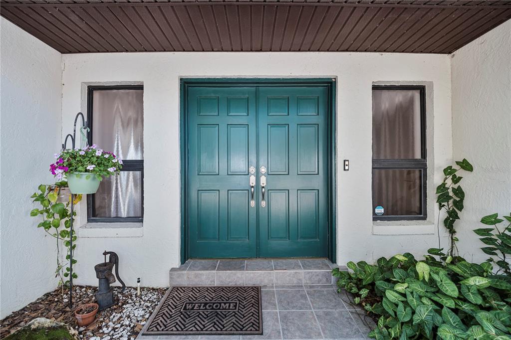 A teal double front door is centered between two windows on a white exterior wall — 11210 ELDERBERRY COURT, CLERMONT, FL