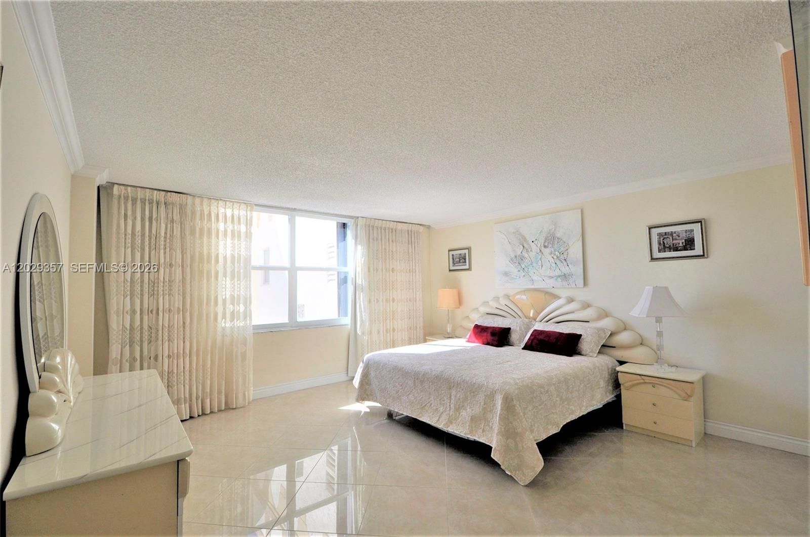 A bedroom features a large bed with a decorative headboard, tile floors, and sheer curtains — 1865 S Ocean Dr # 20H, Hallandale Beach FL 33009, HALLANDALE BEACH, FL
