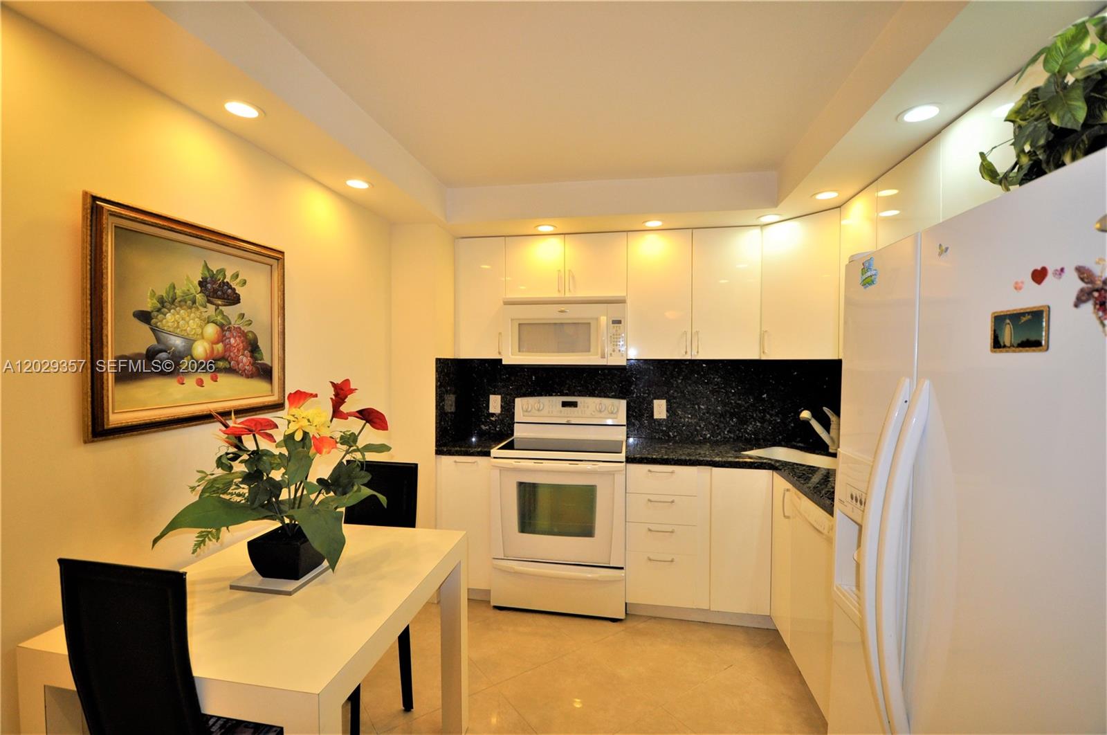 A kitchen features white cabinetry, black granite countertops, a white stove, and a dining table — 1865 S Ocean Dr # 20H, Hallandale Beach FL 33009, HALLANDALE BEACH, FL