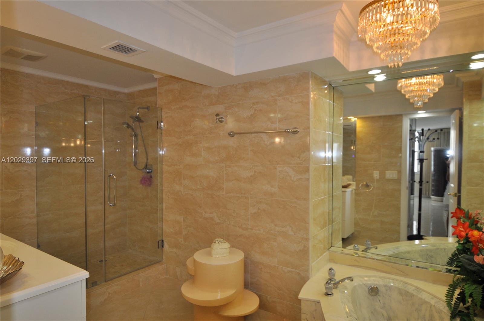 A bathroom features beige tile walls, a glass-enclosed shower, a soaking tub, and a chandelier — 1865 S Ocean Dr # 20H, Hallandale Beach FL 33009, HALLANDALE BEACH, FL