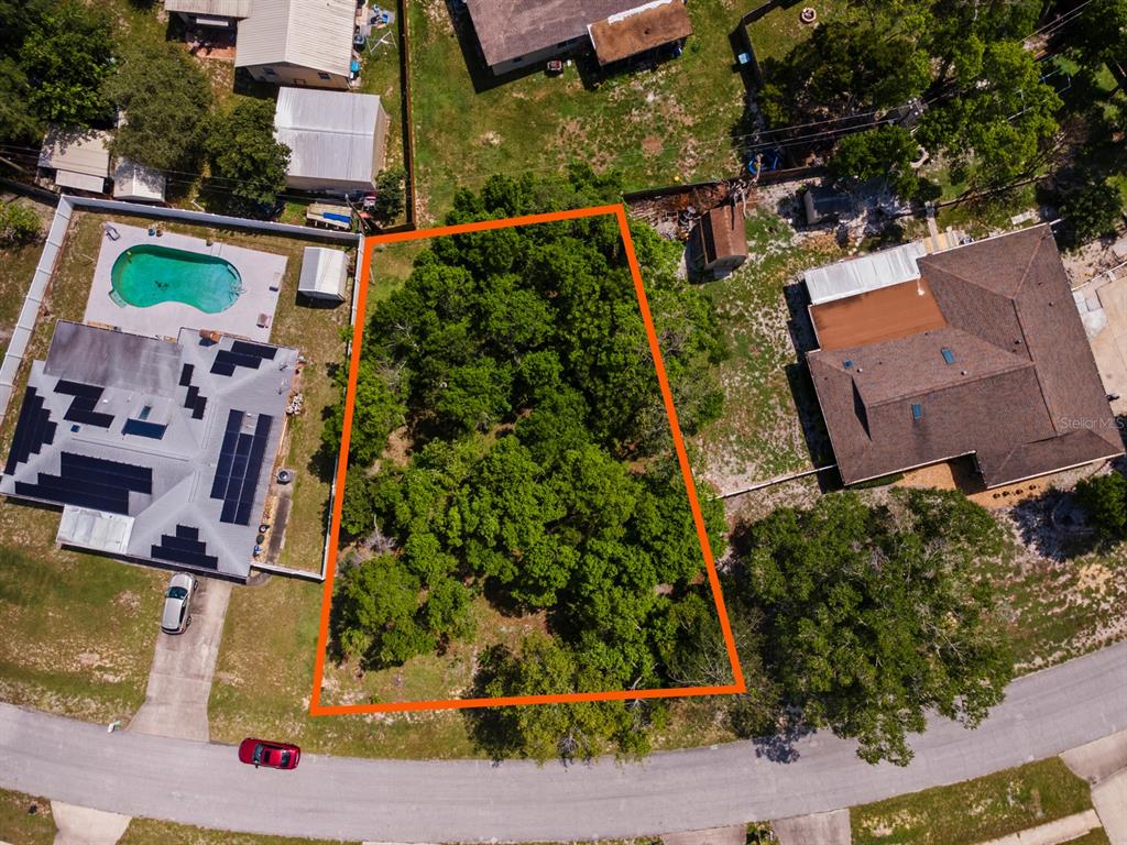 An aerial view shows a vacant, tree-covered lot outlined in orange between two residential properties — 1041 FEATHER DRIVE, DELTONA, FL