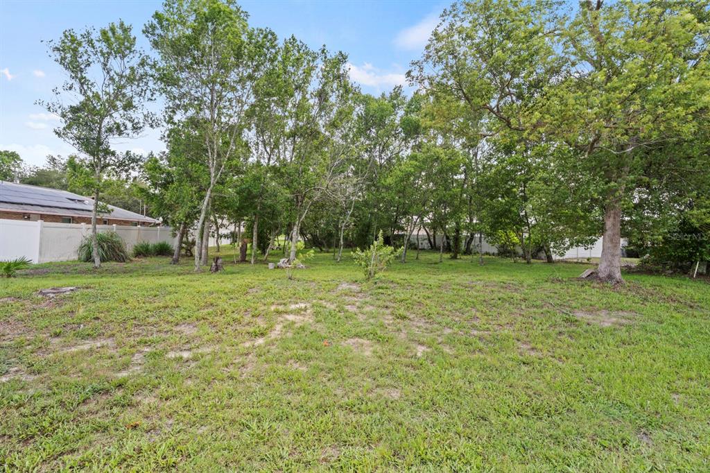 A grassy backyard features scattered trees and a white vinyl fence along the perimeter — 1041 FEATHER DRIVE, DELTONA, FL