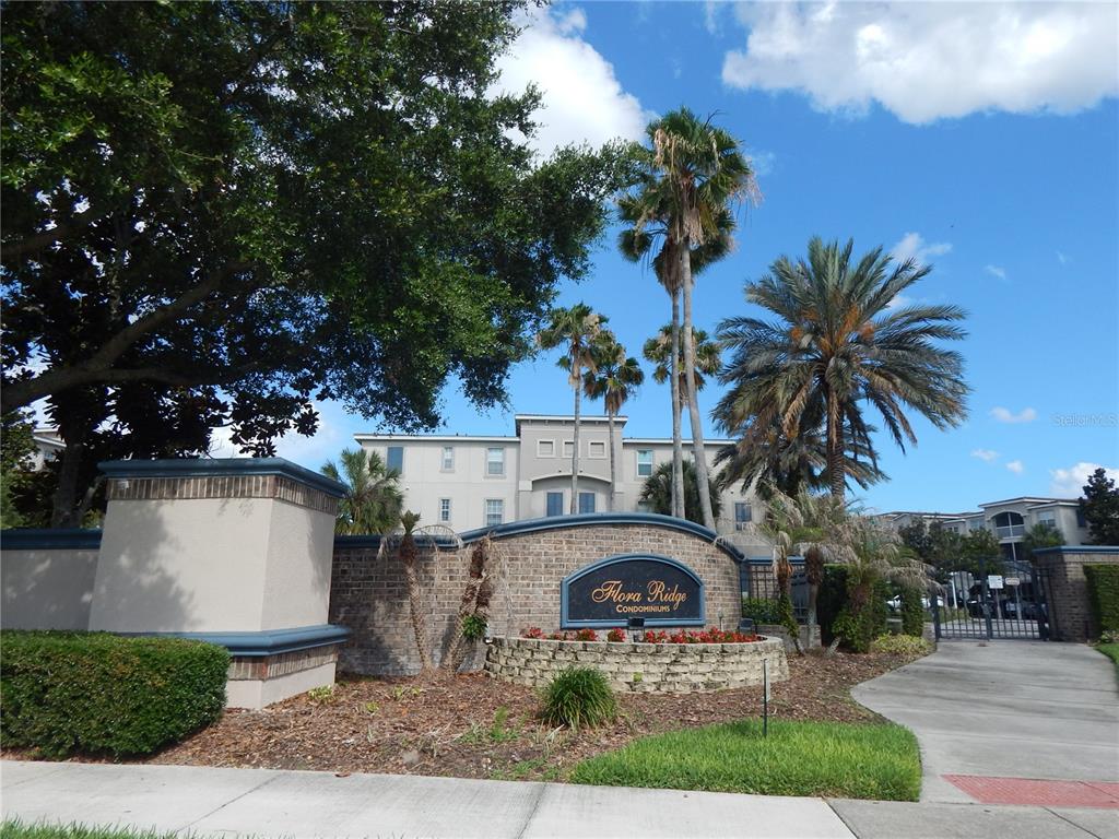 The exterior of the Flora Ridge Condominiums features a brick entrance sign and palm trees — 3300 WHITESTONE CIRCLE UNIT 107, KISSIMMEE, FL